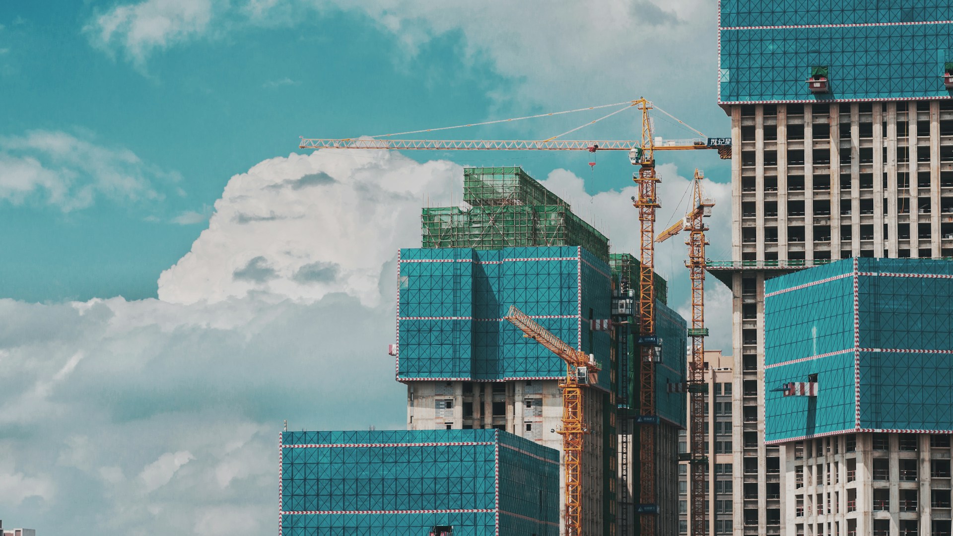 Construction cranes above new buildings under a blue sky